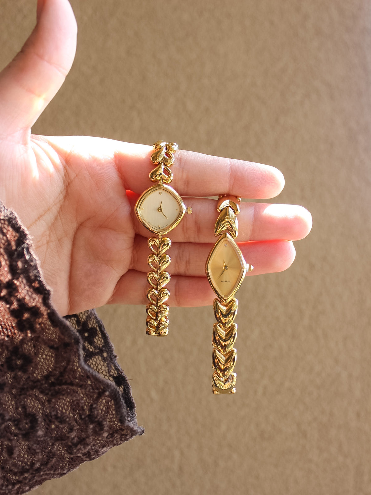 A pair of gold-toned watches set held in a person's hand against a warm beige background.