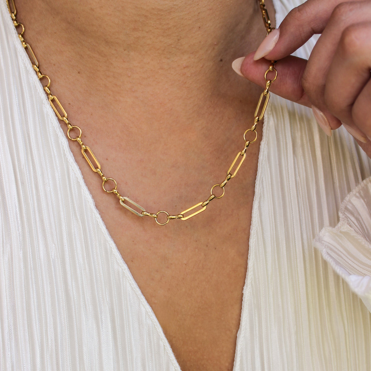Gold chain necklace being adjusted on a person wearing a white top.