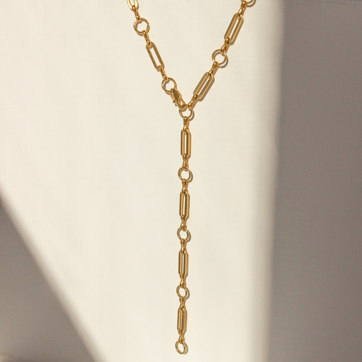 Gold chain necklace on a white surface with soft shadows