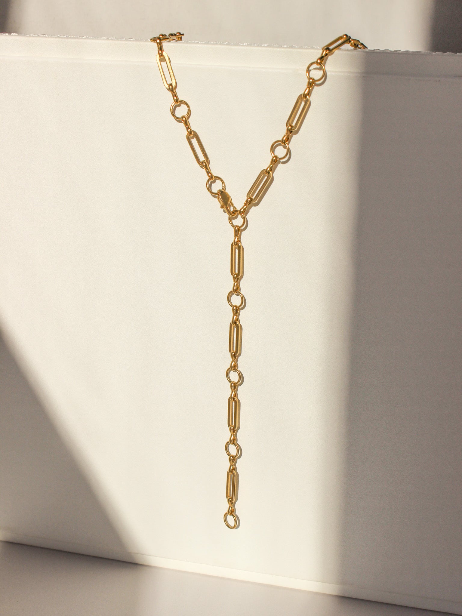 Gold chain necklace on a white surface with soft shadows