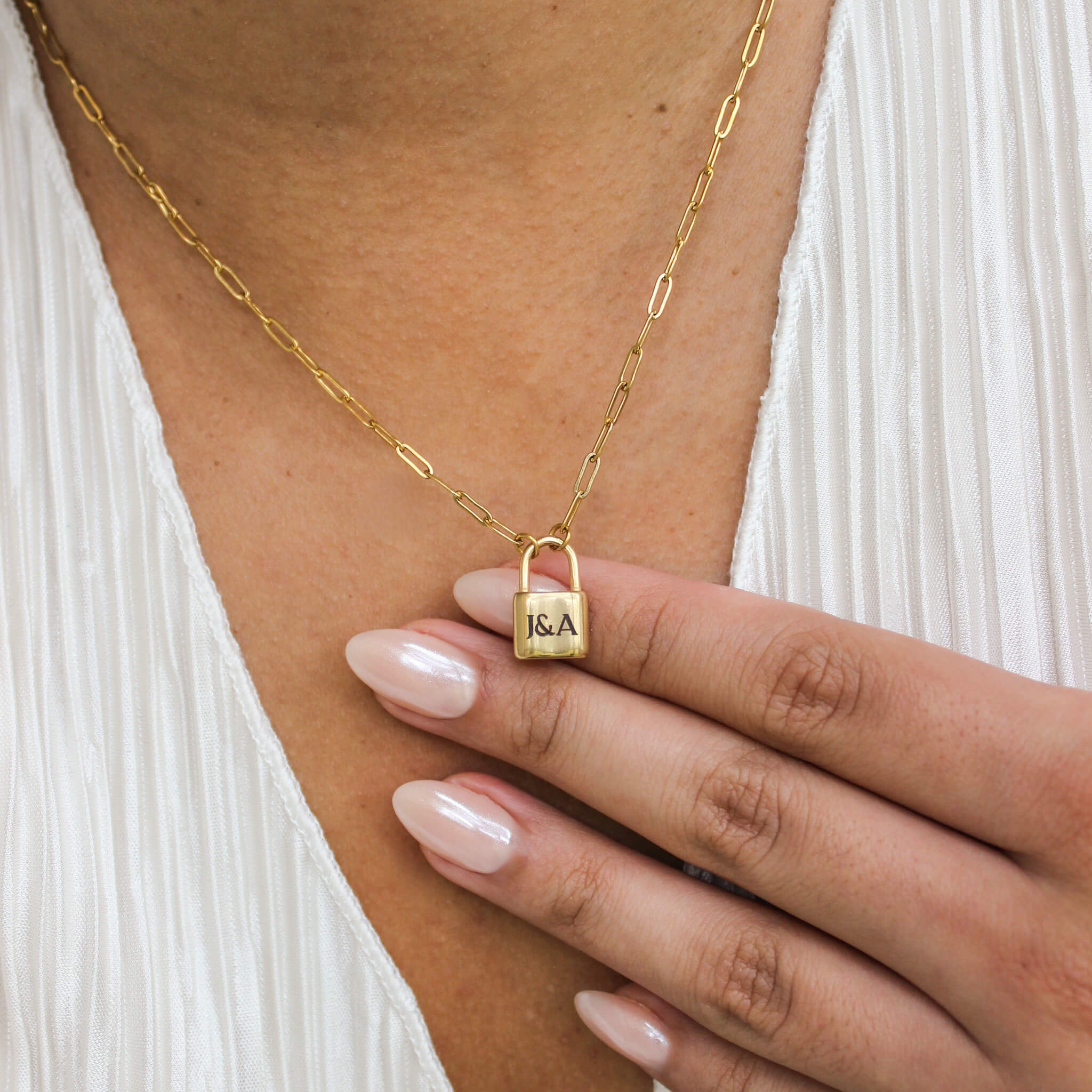 Gold necklace with a lock pendant worn by a person, close-up of hand and necklace.