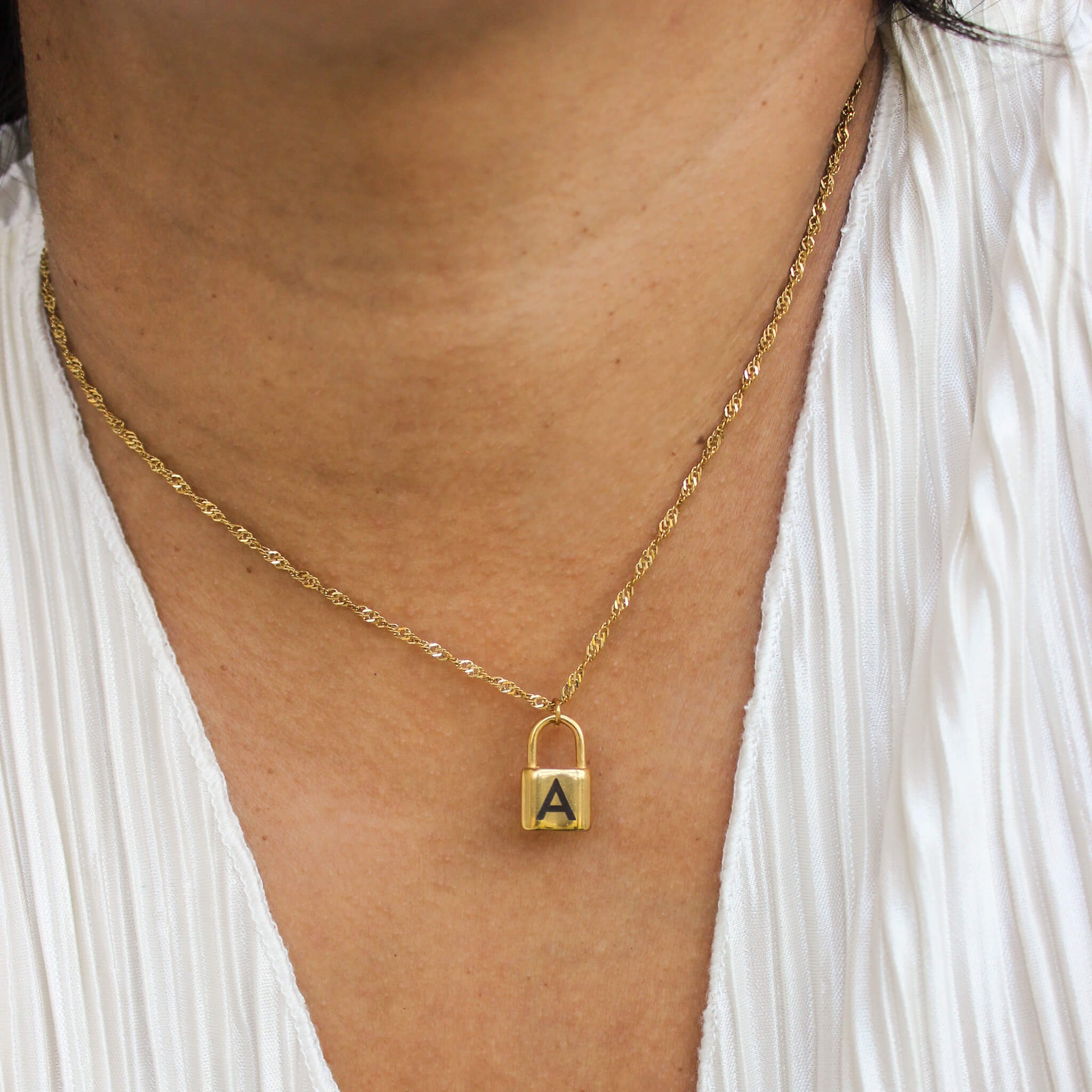 Gold necklace with a lock-shaped pendant on a person wearing a white top.