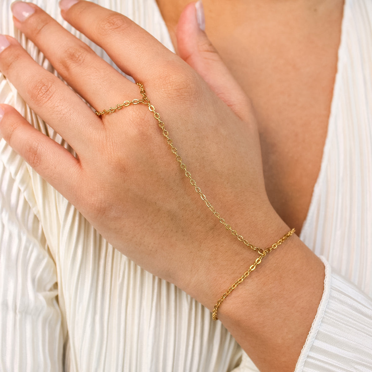 Gold hand chain worn on a hand with a white garment background