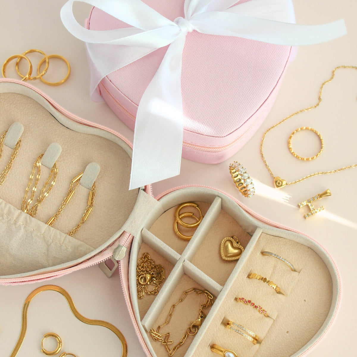 Heart-shaped jewelry box with gold jewelry and a white ribbon on a beige background