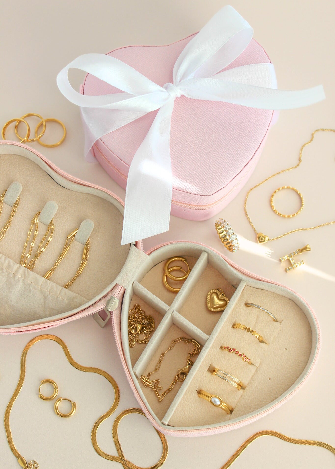 Heart-shaped jewelry box with gold jewelry and a white ribbon on a beige background