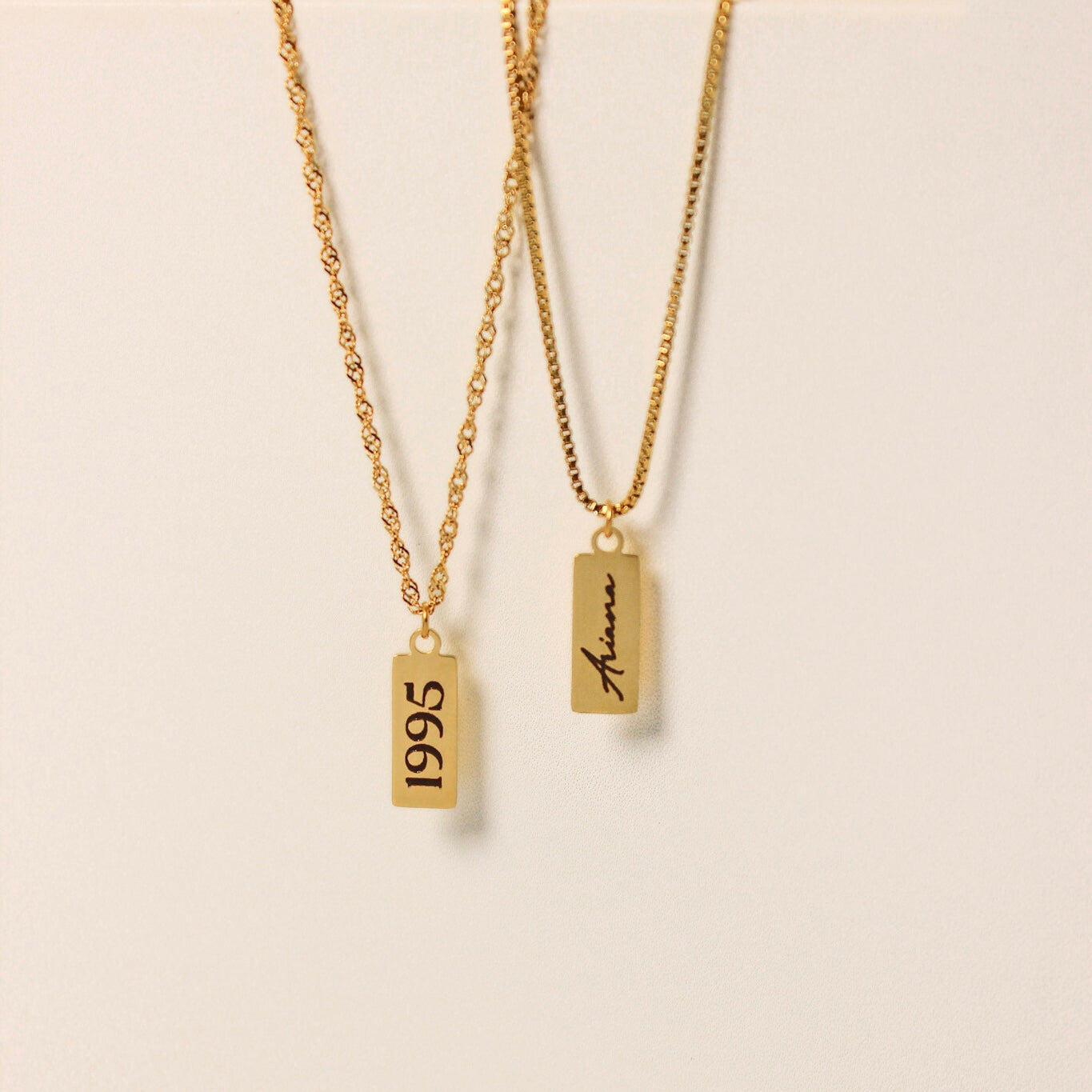 Two gold necklaces with engraved text on a beige background