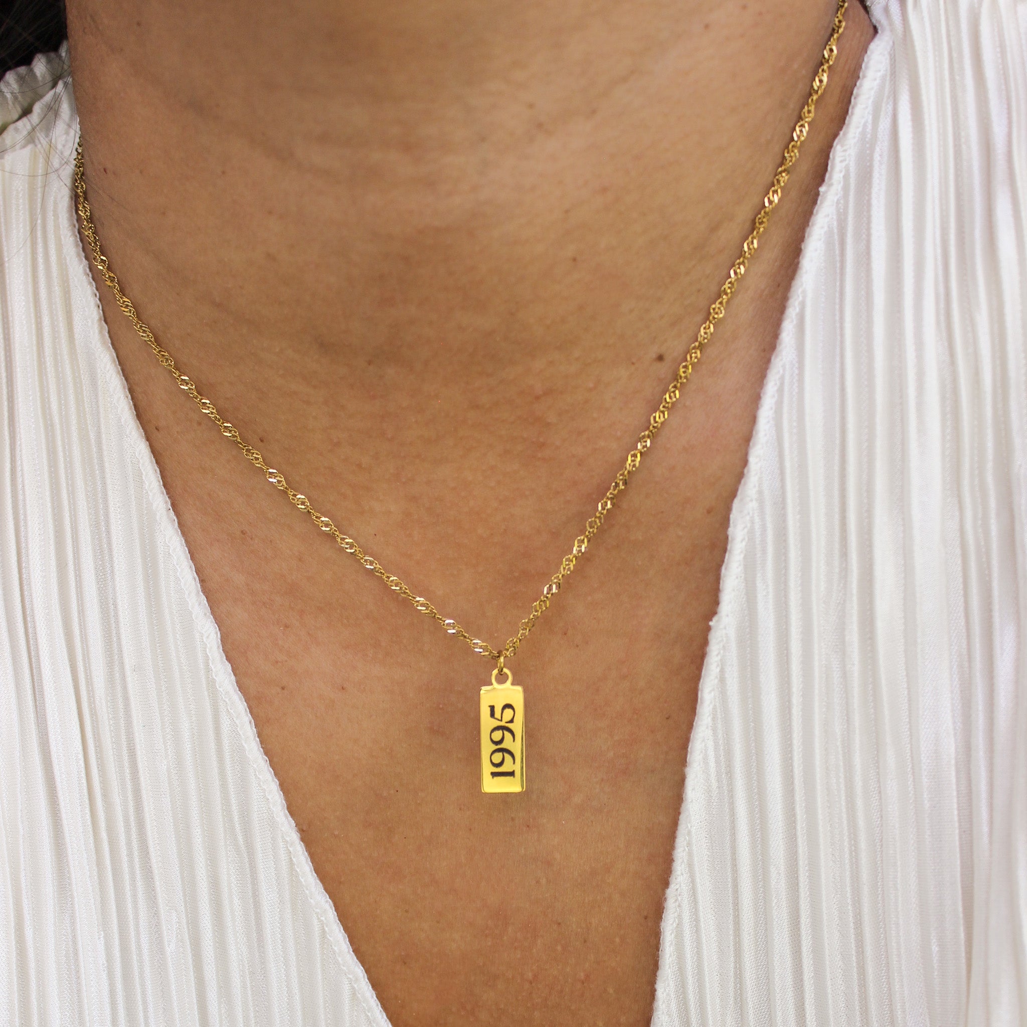 Gold necklace with a '1995' pendant worn by a person against a white background