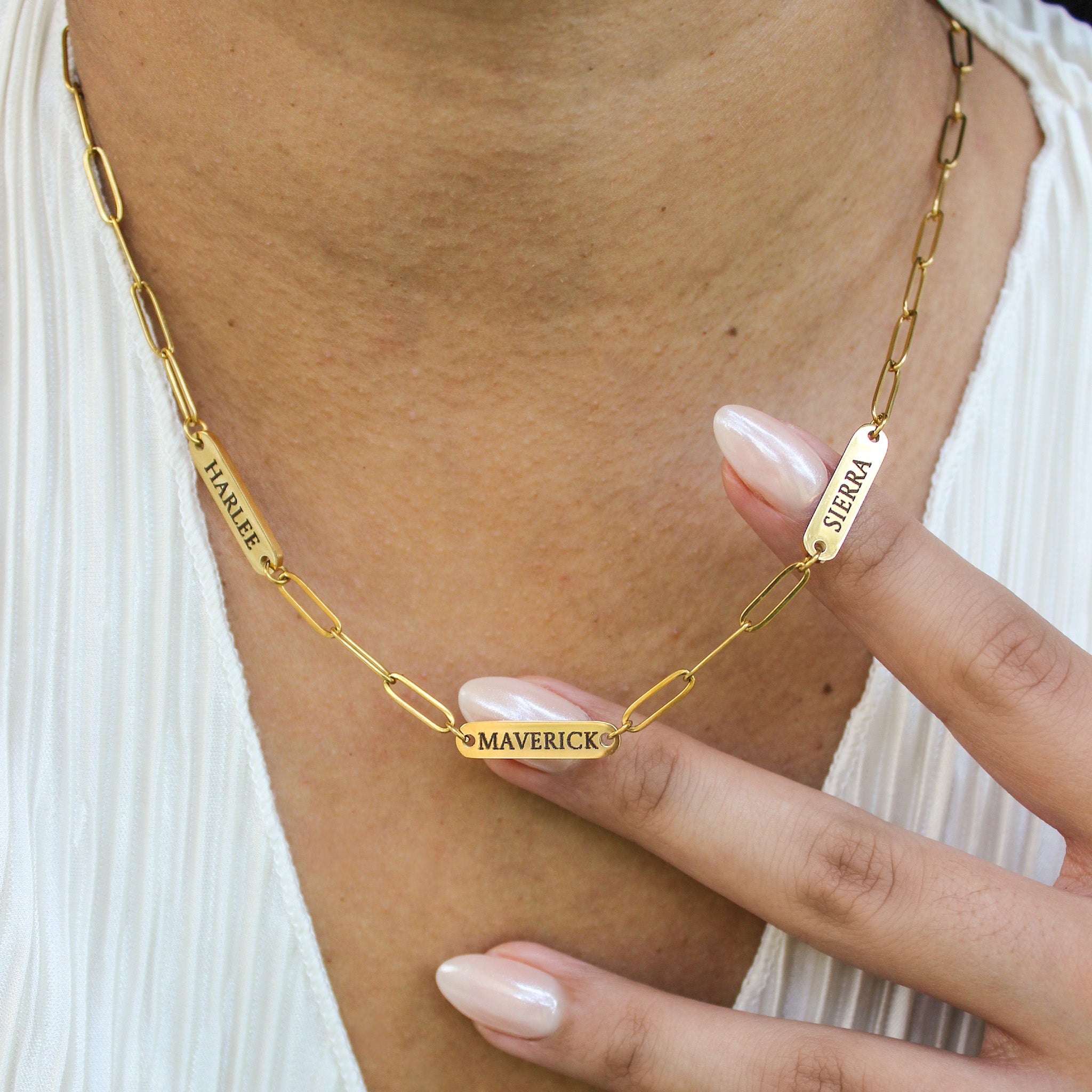 Gold chain necklace with engraved names, worn by a person.