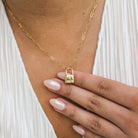 Gold necklace with a lock pendant worn by a person, close-up of hand and necklace.