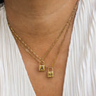 Gold necklace with lock pendants on a person wearing a white top