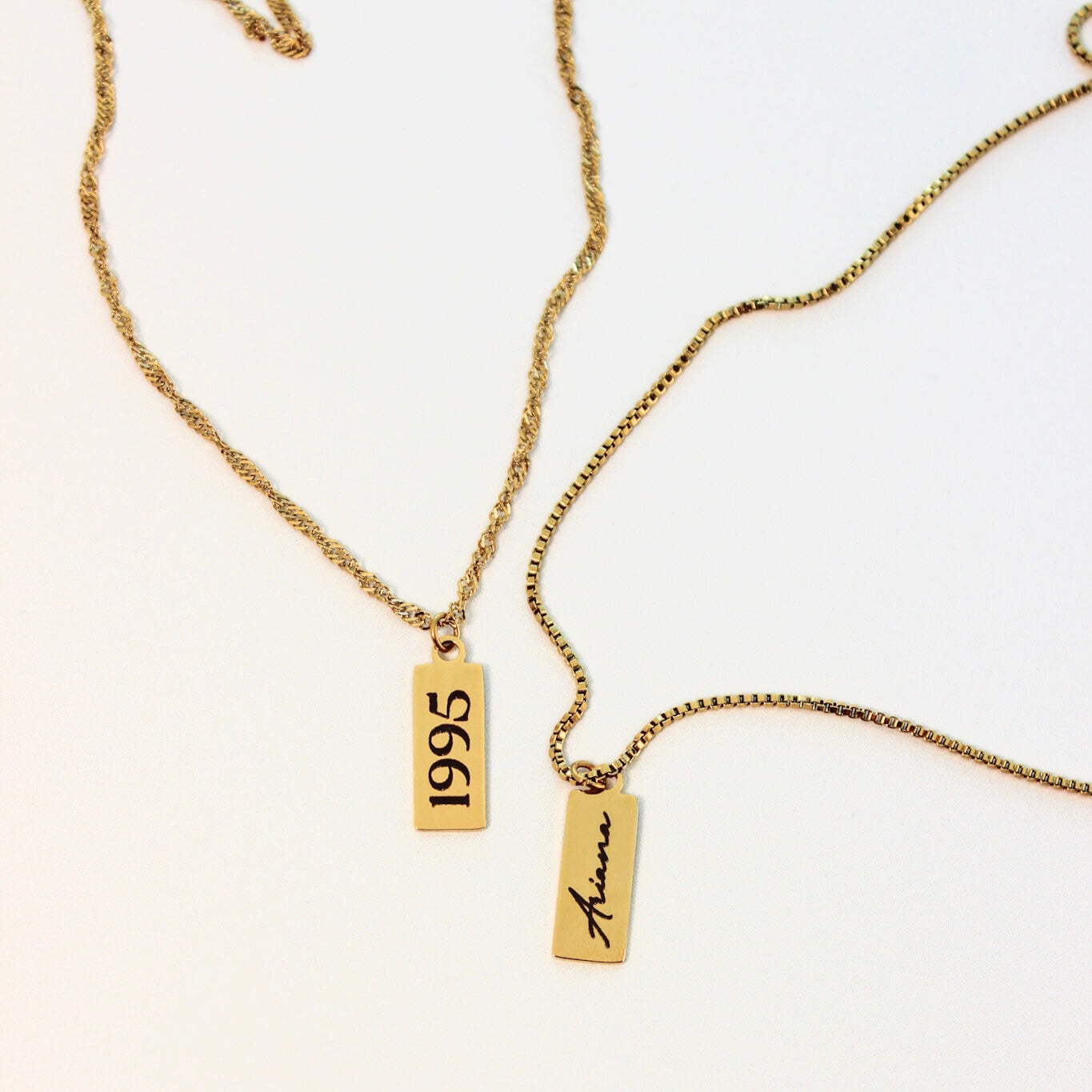 Gold necklaces with '1995' and 'Ariana' tags on a white background