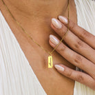 Gold necklace with a name pendant on a person wearing a white top.