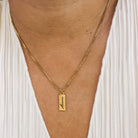 Gold necklace with a pendant on a person wearing a white dress.