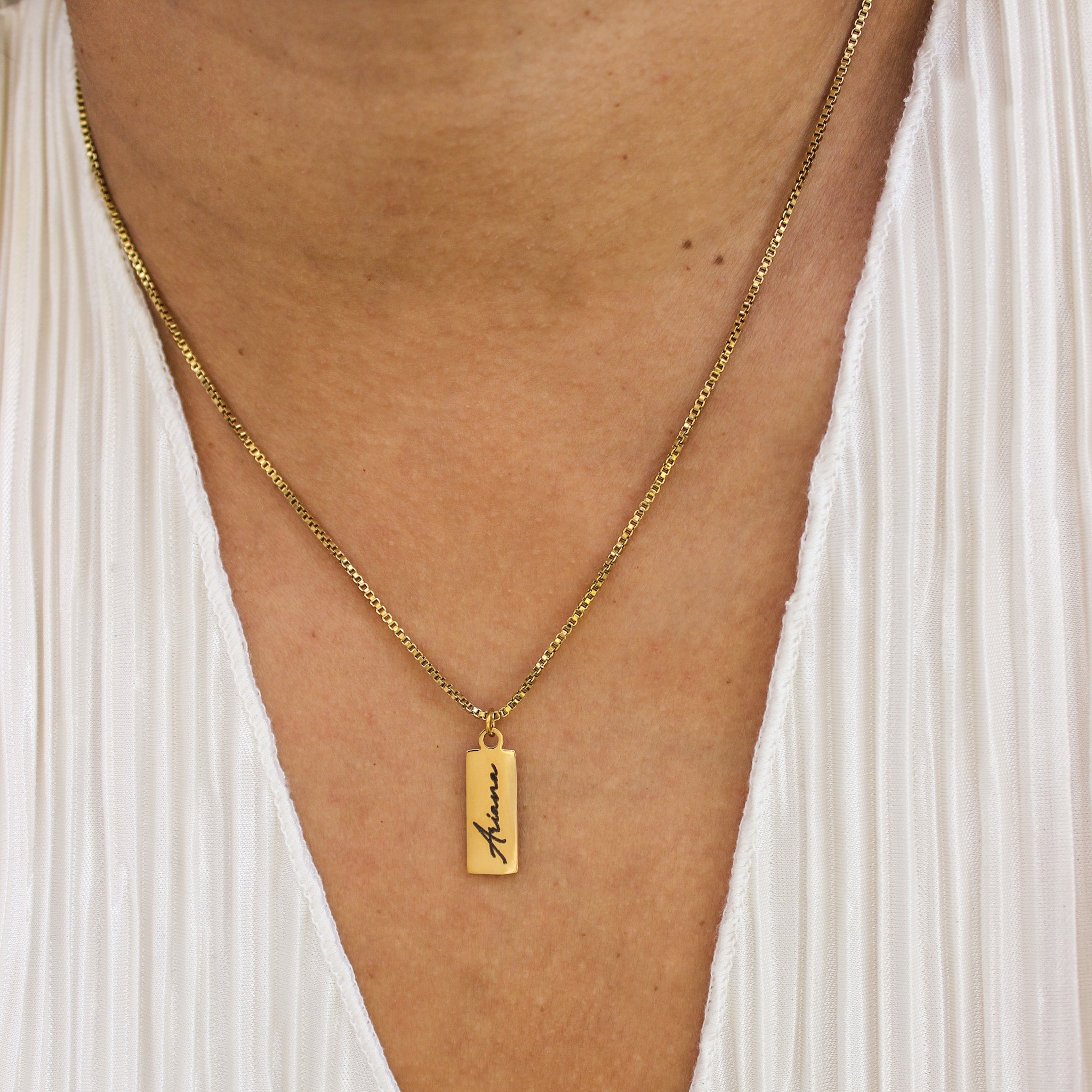 Gold necklace with a pendant on a person wearing a white dress.