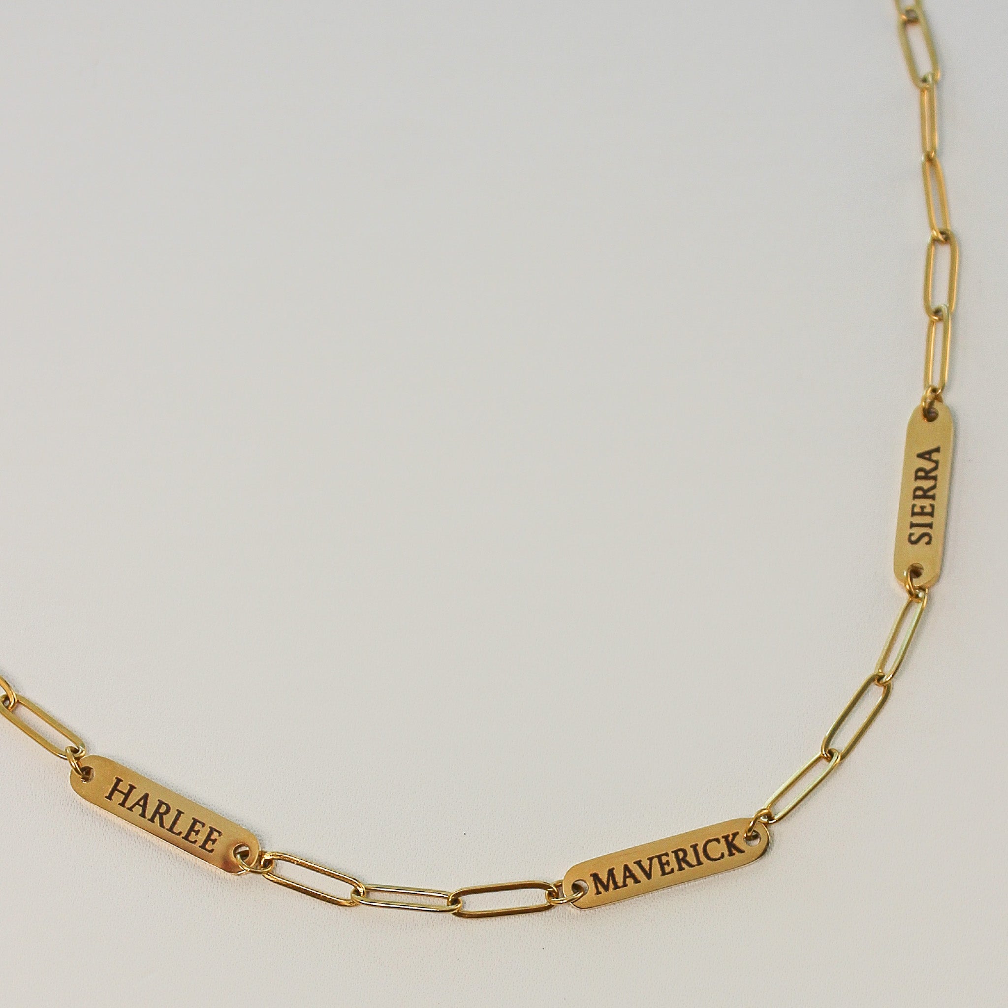 Gold chain bracelet with engraved names on a light gray background